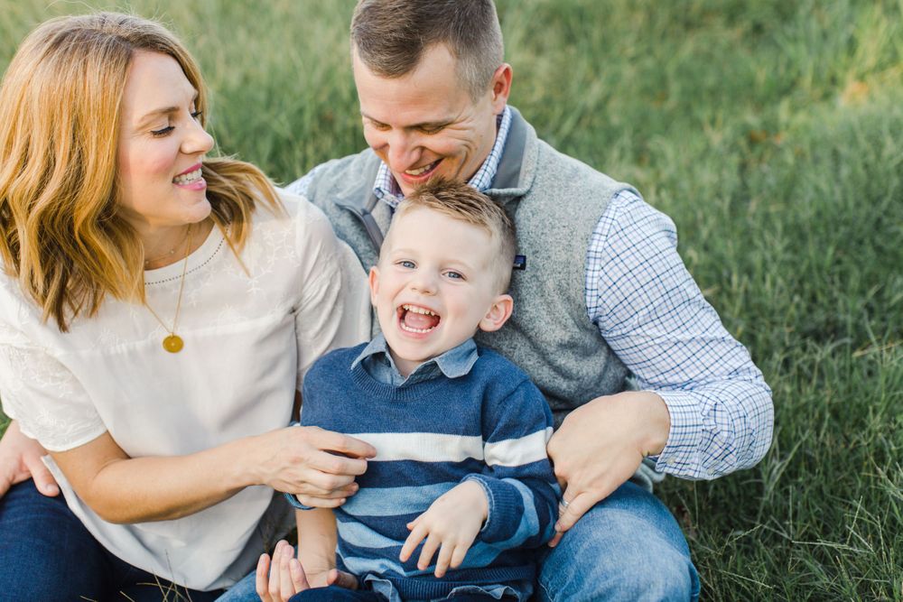 Joyful family moment shared on grass with genuine laughter and natural expressions.