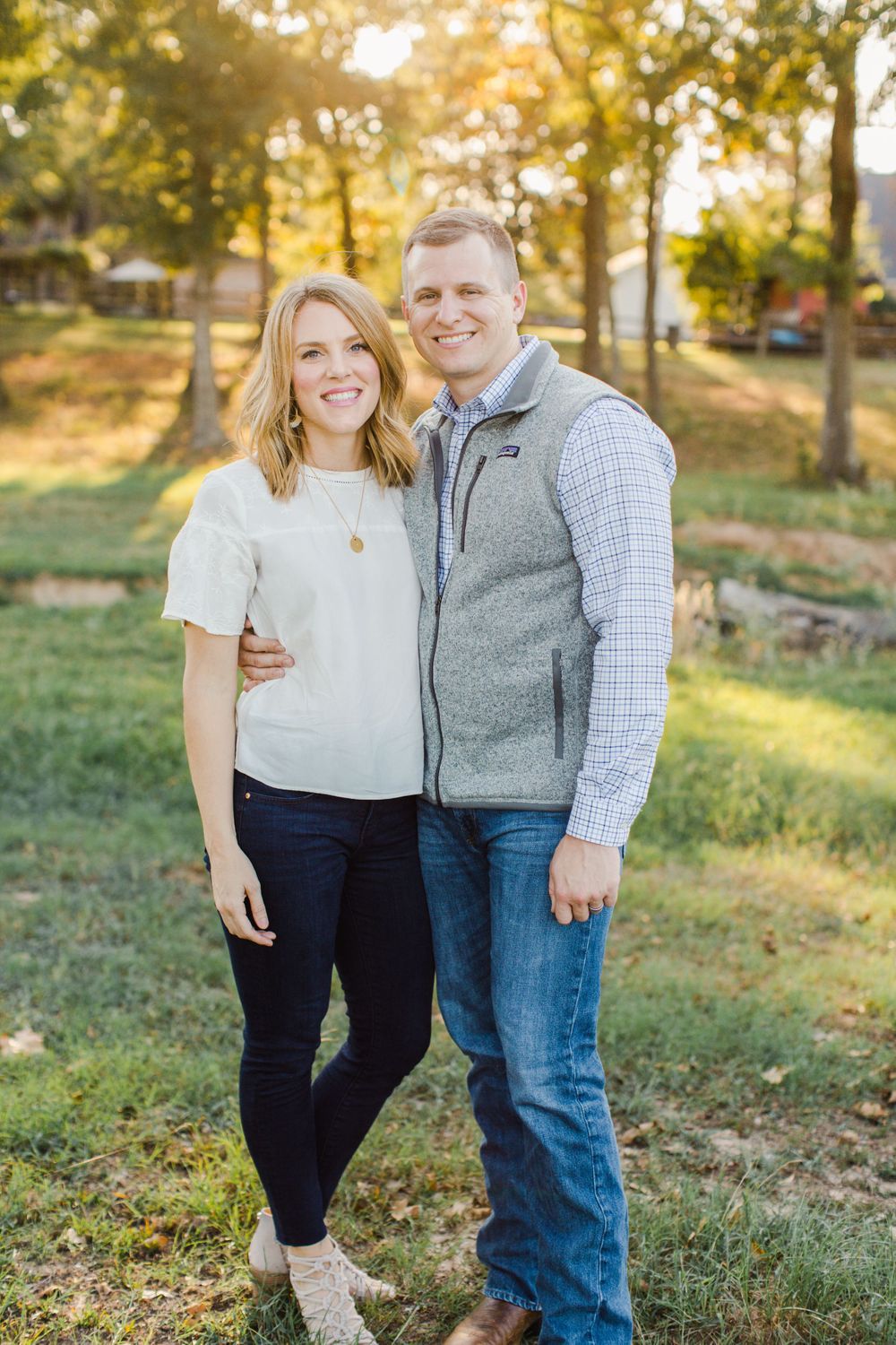 Casual outdoor couple portrait with autumn trees and warm sunlight in background.