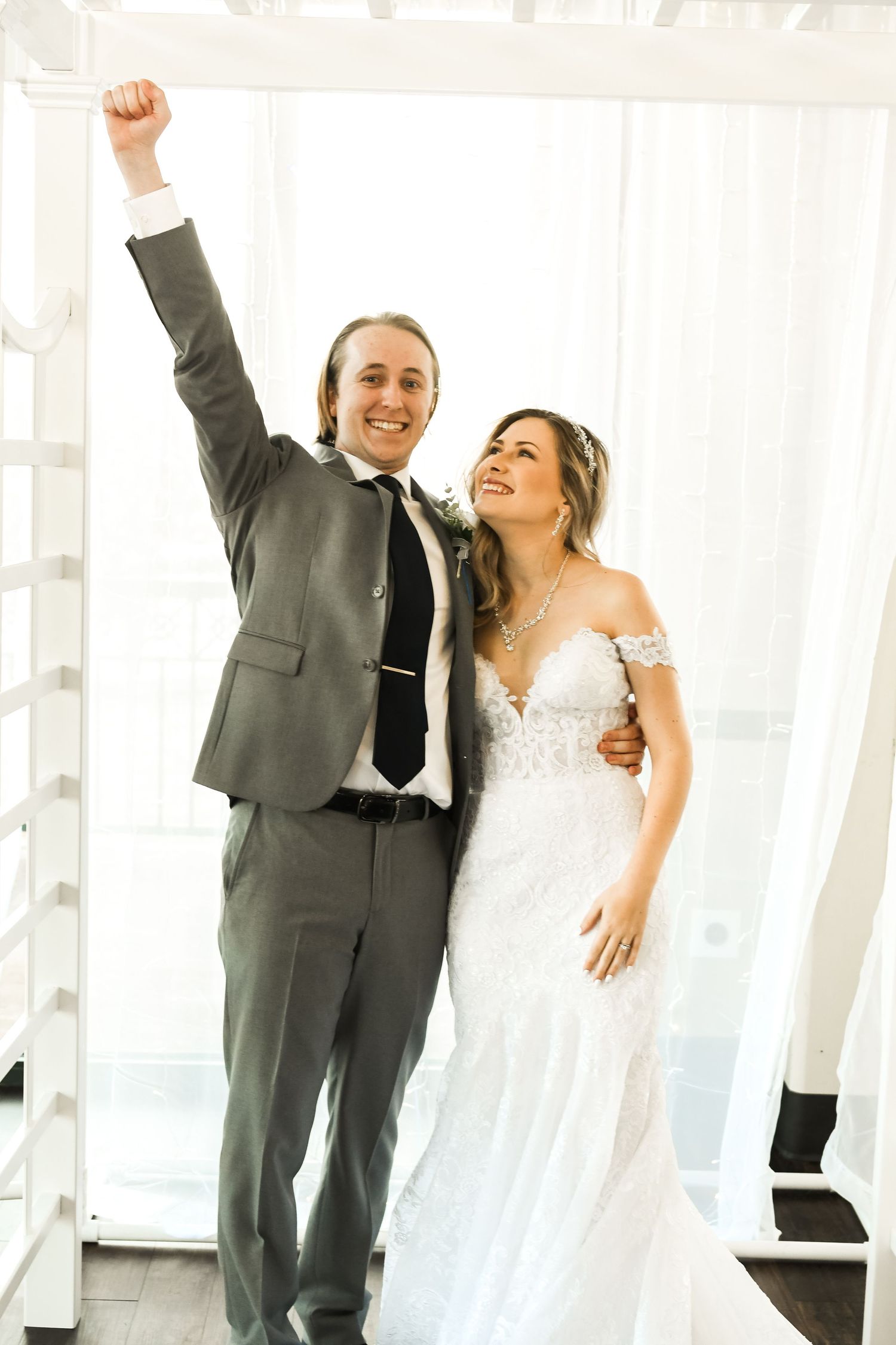 Newlyweds celebrate joyfully in a bright indoor venue with the groom raising his fist triumphantly.