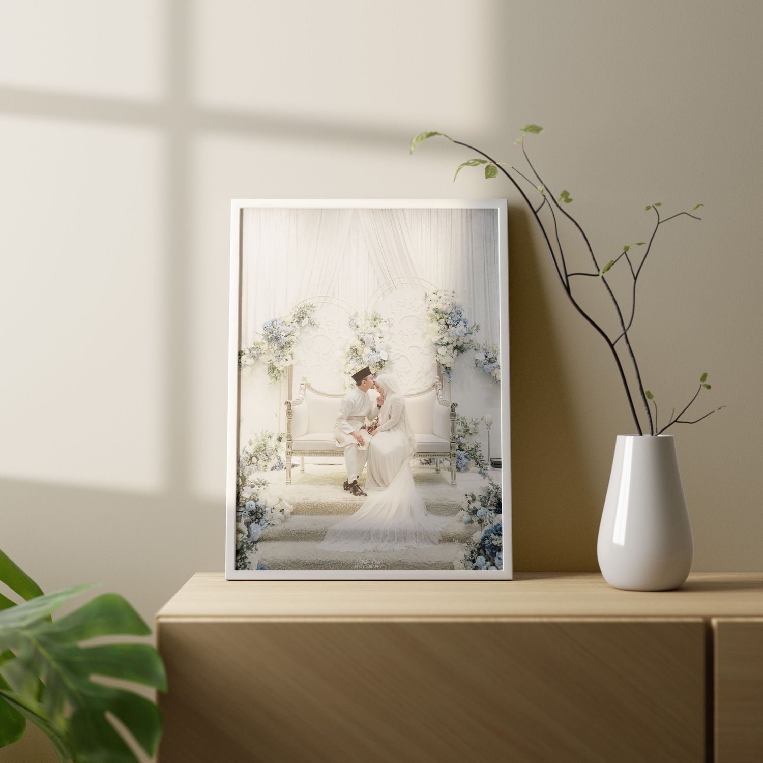 Wedding photo display on wooden shelf with white ceramic vase and window light.