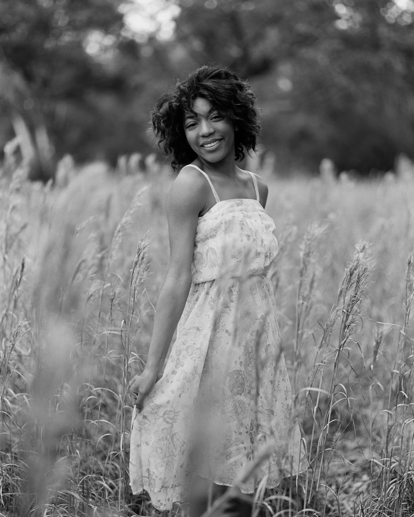 Black and white portrait of someone in a sundress standing in a field of tall grass.