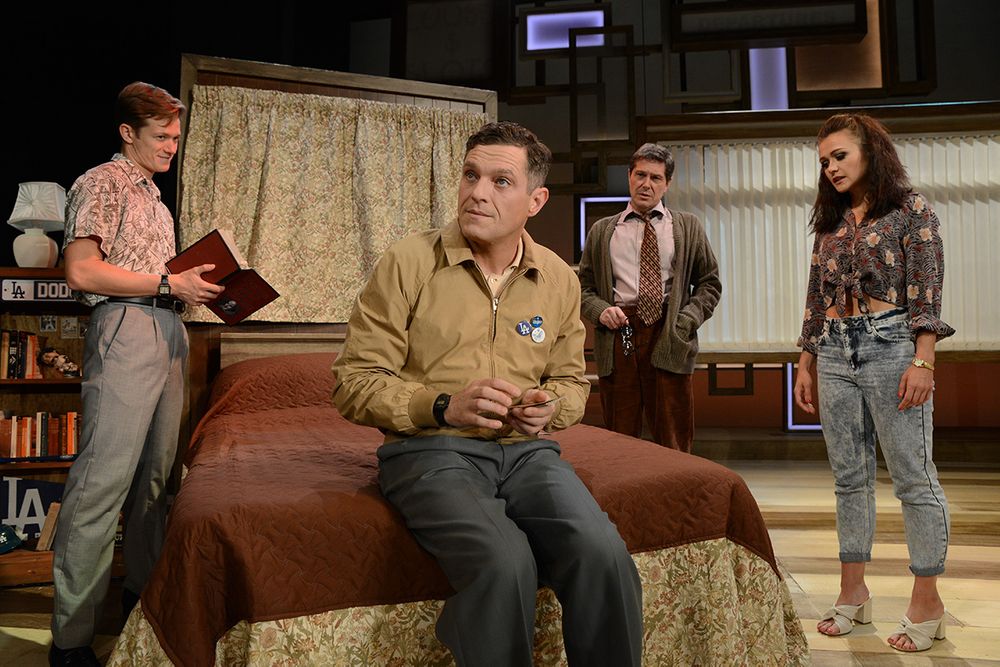 A staged living room scene with actors positioned around a brown leather couch.