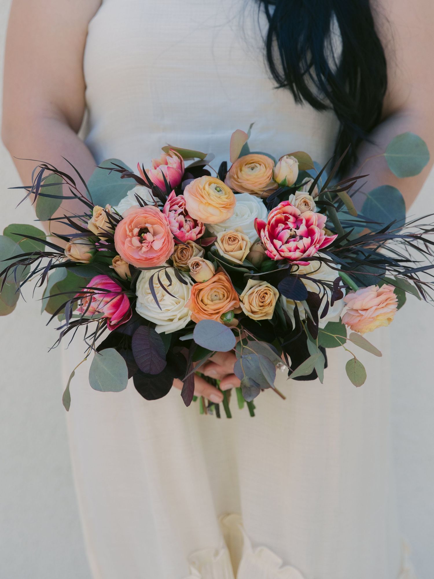 Elegant wedding bouquet featuring pink and peach roses with eucalyptus leaves against white background.