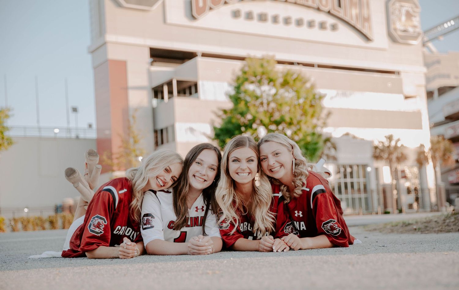 Group of college graduates lean in and smile in front of their campus football stadium.