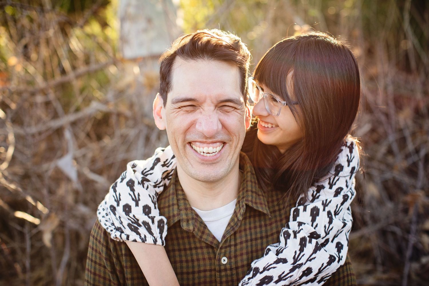 Couple sharing a candid laughing moment outdoors in natural lighting.