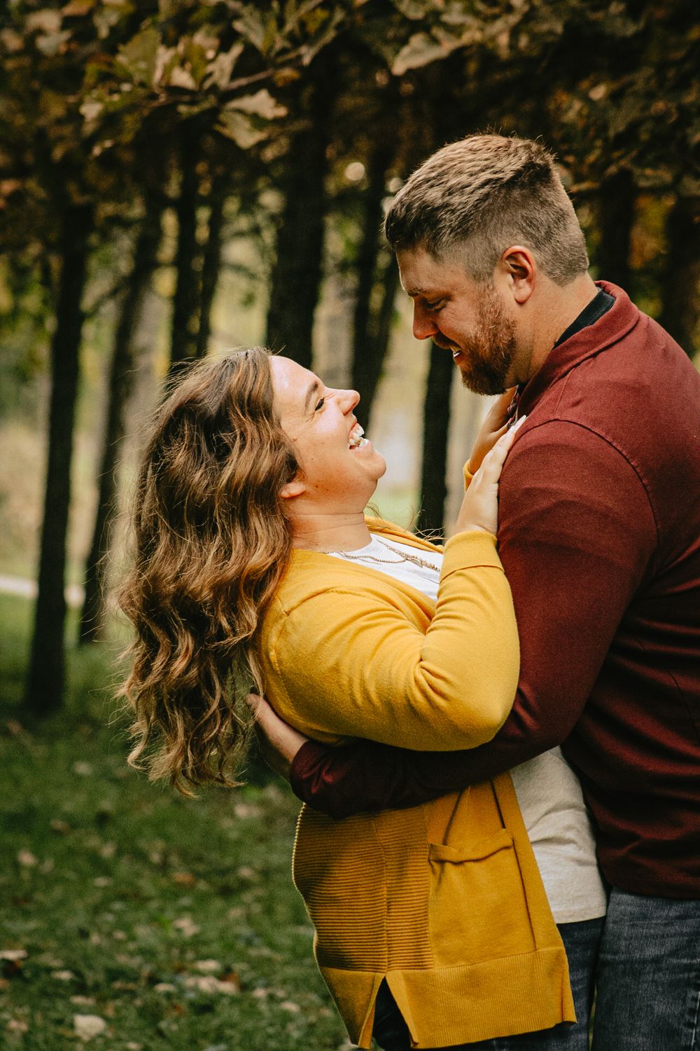 A joyful couple in yellow and burgundy embracing outdoors during fall.