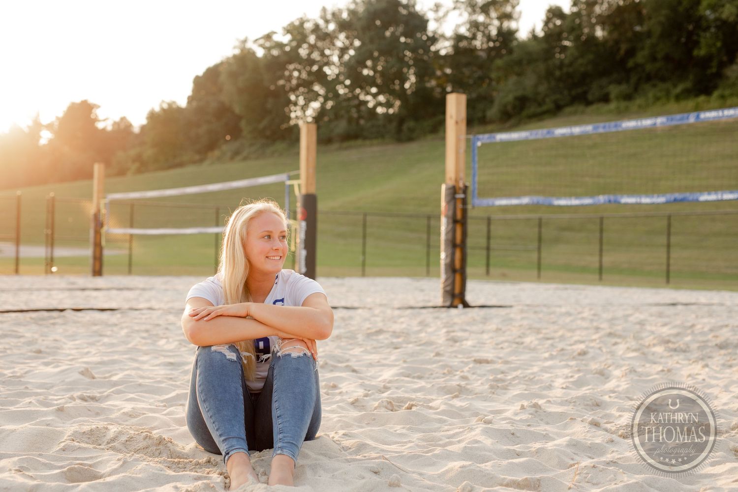 Player sitting contemplatively on sand volleyball court at sunset.