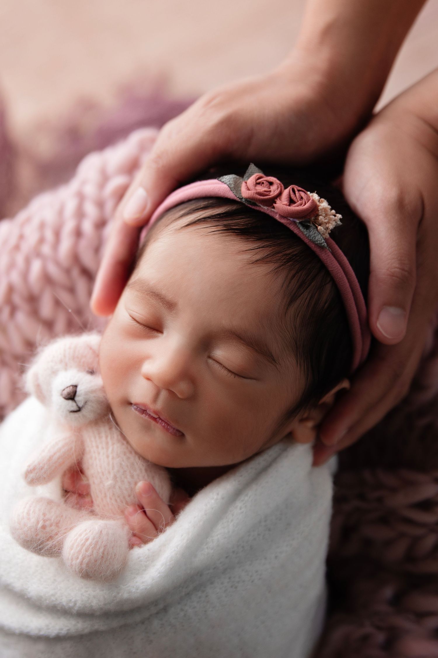 Sleeping newborn with pink floral headband wrapped in white during photo session.