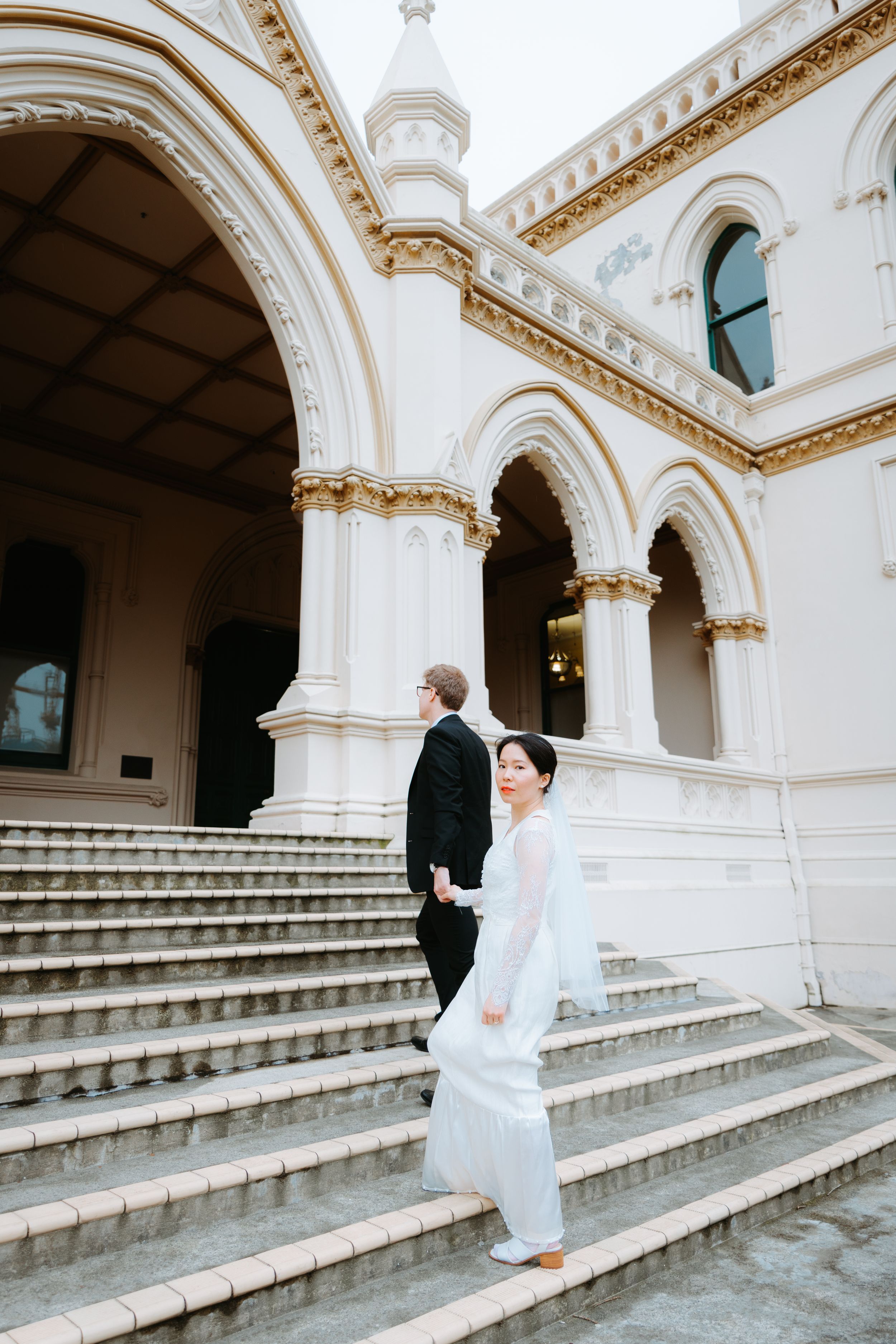 Couple walking down ornate marble steps of a historic Wellington building - cinematic wedding photo by Selah Weddings.
