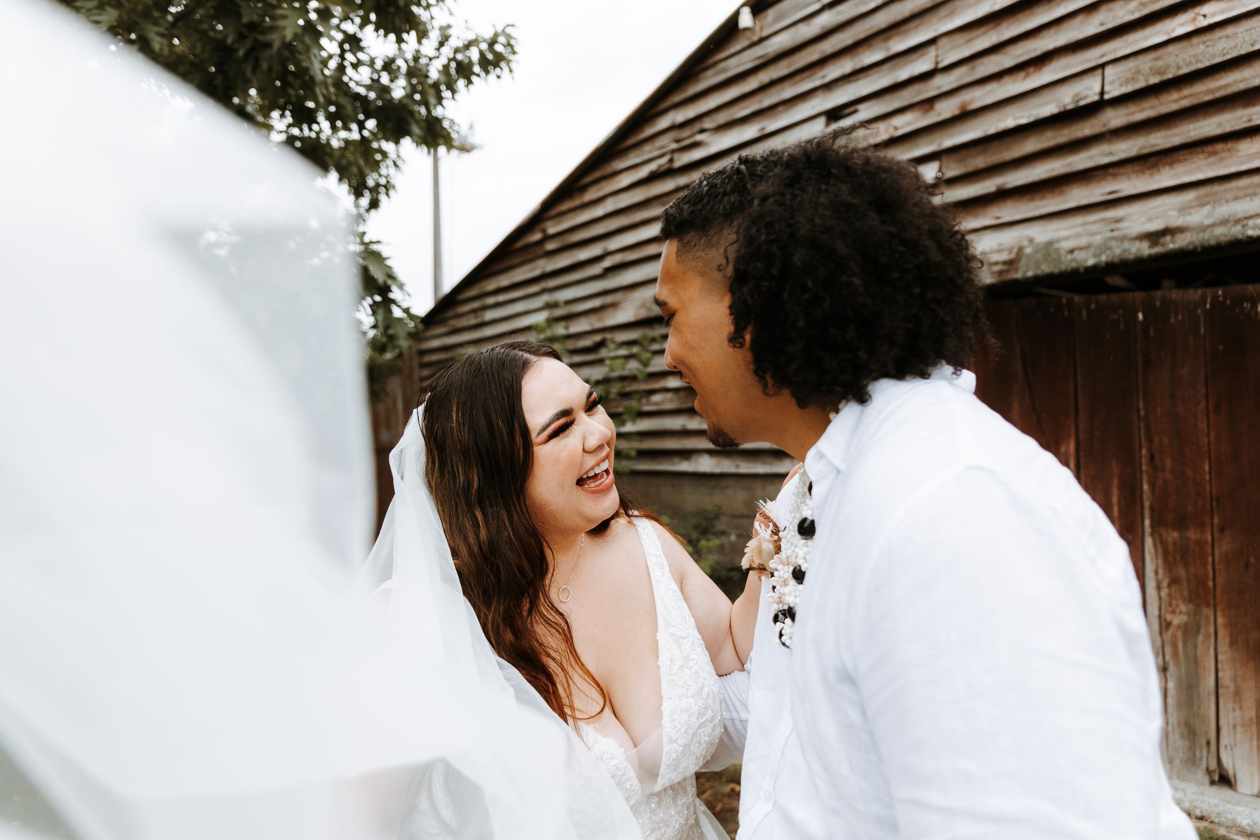 close up of bride and groom laughing with each other, in palmerston north, her veil is in the foreground. photos by selah weddings nz.