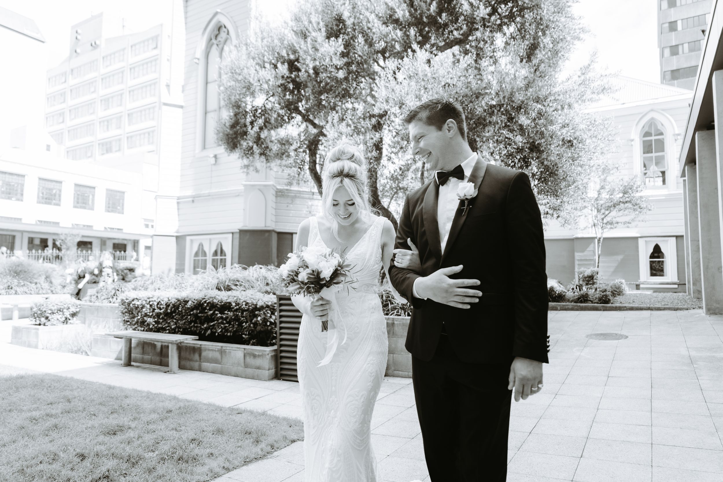 Black-and-white image of a couple walking outside a Palmerston North church - documentary-style wedding photography.