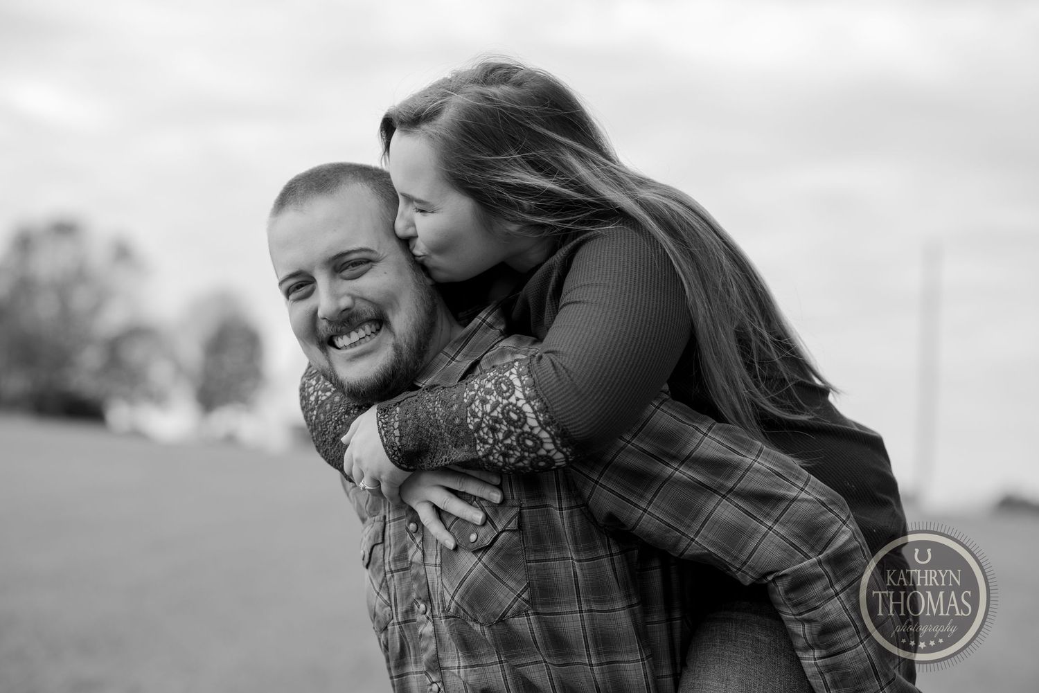 A black and white portrait of a couple sharing a joyful piggyback moment outdoors.