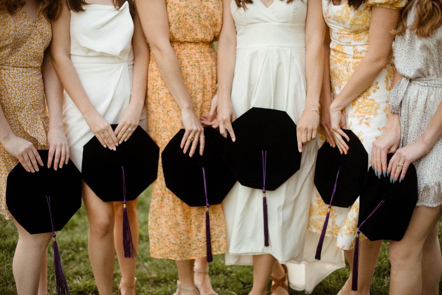 Close-up of hands holding black graduation caps against floral dresses.