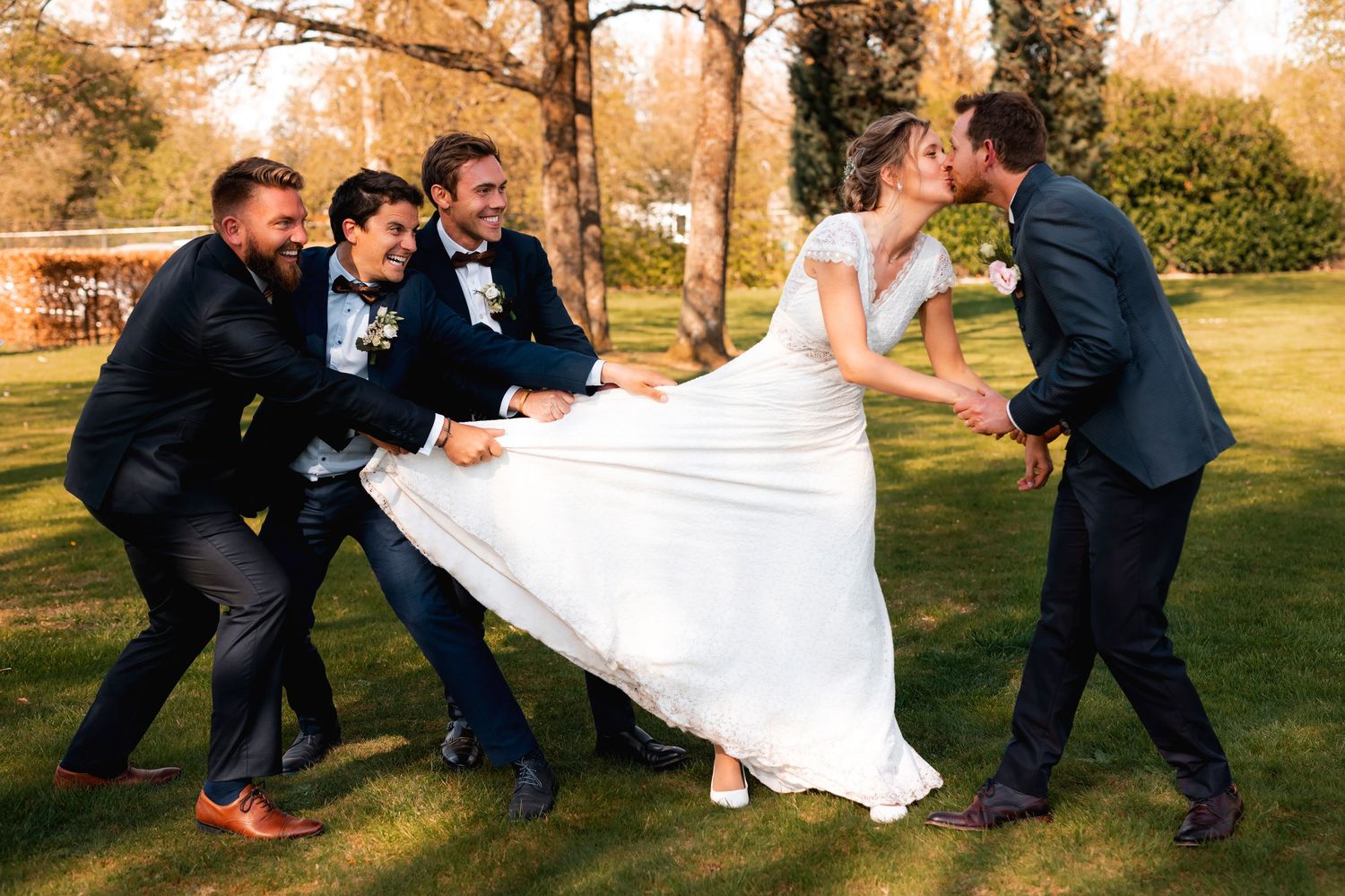 Playful wedding party lifts the bride's dress while posing outdoors.