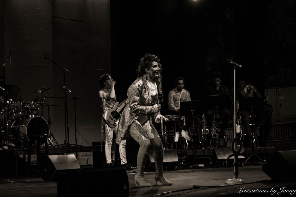 Black and white photo of an energetic performer dancing on stage with a live band.