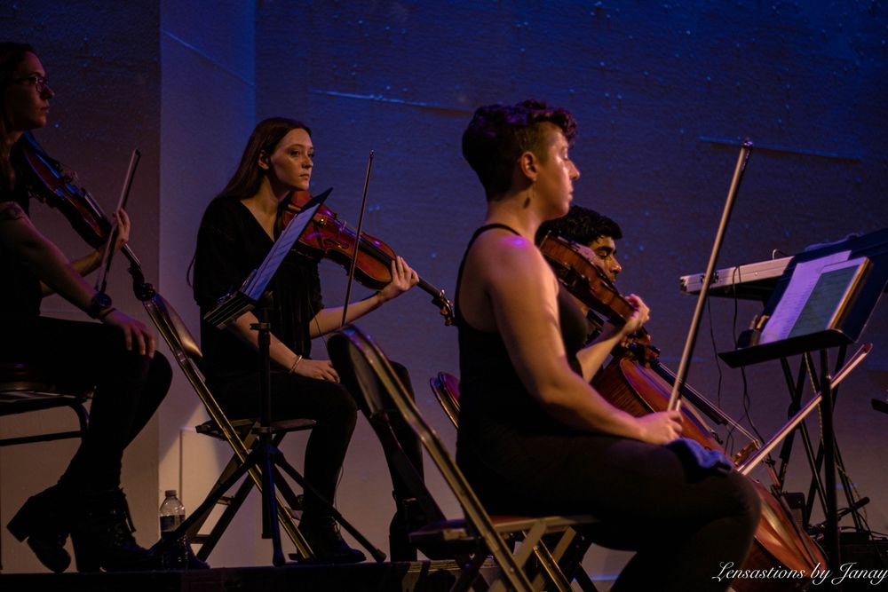 String quartet performers in black attire playing violins and cello on a dimly lit stage.