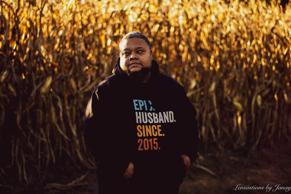 Man in an Epic Husband Since 2015 hoodie standing in front of a golden cornfield.