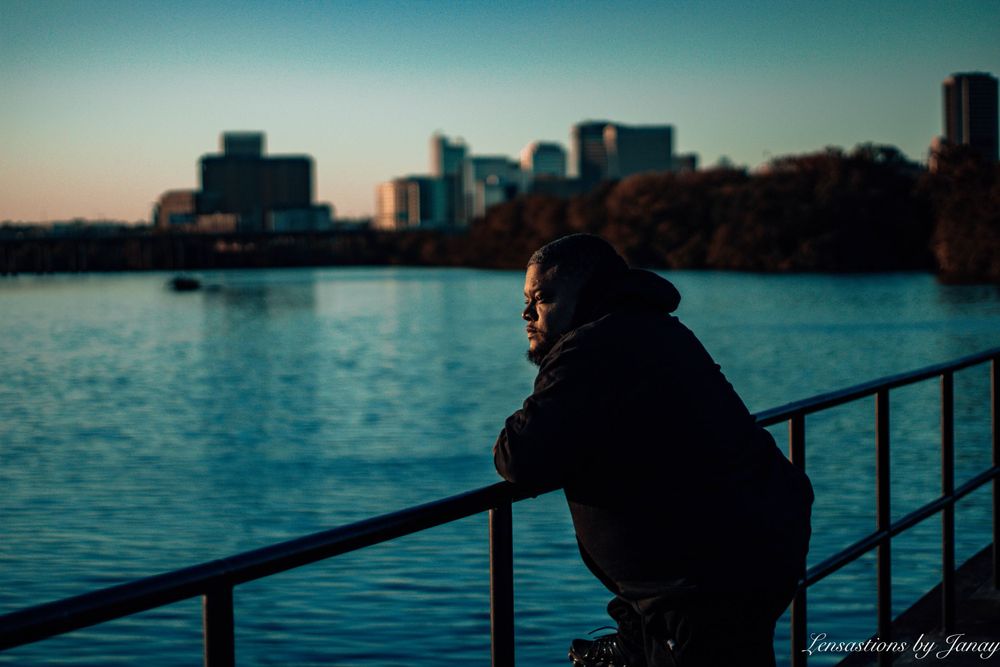 Person leaning on railing overlooking a city skyline at dusk near a calm river.