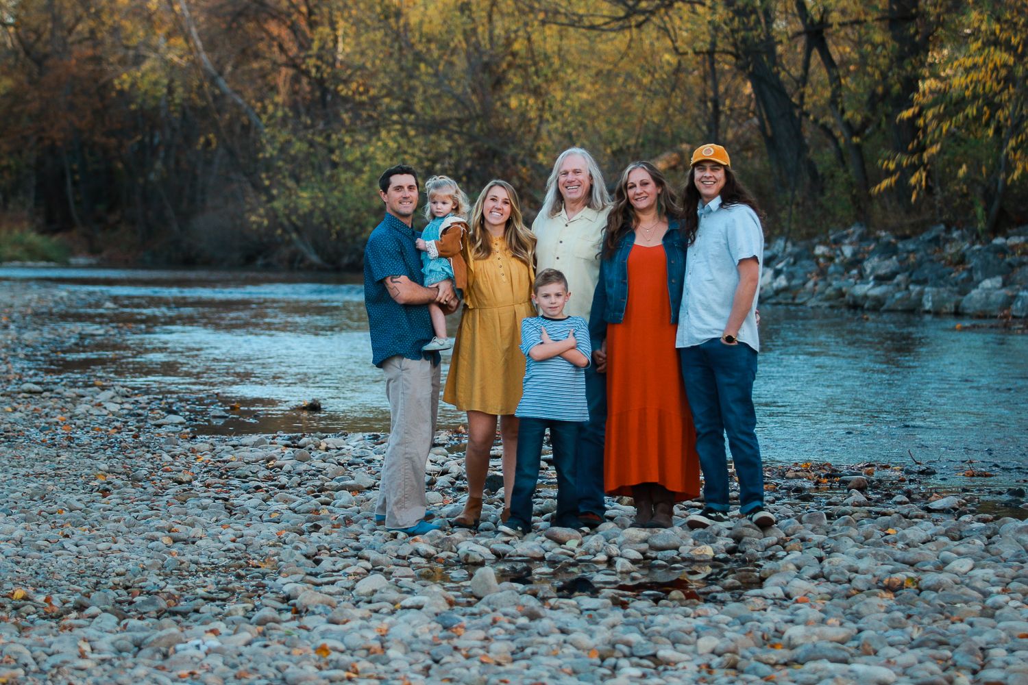 Extended family gathering on a riverbank during autumn season.