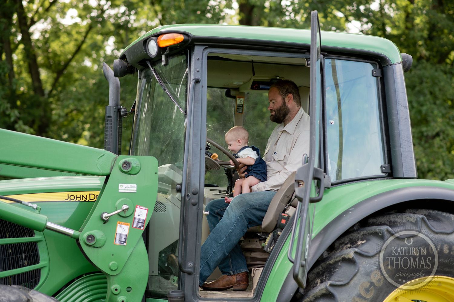 A view through the window of a John Deere tractor showing two people inside the cab.