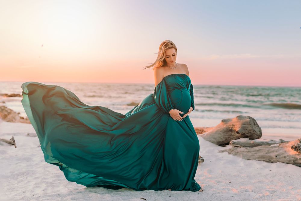 Woman in green maternity dress holding her belly at beach