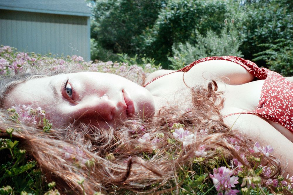 A dreamy portrait of someone lying in pink wildflowers wearing a red dress.