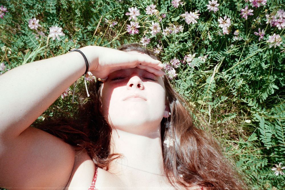 A summery portrait showing someone shielding their eyes from bright sunlight among flowers.