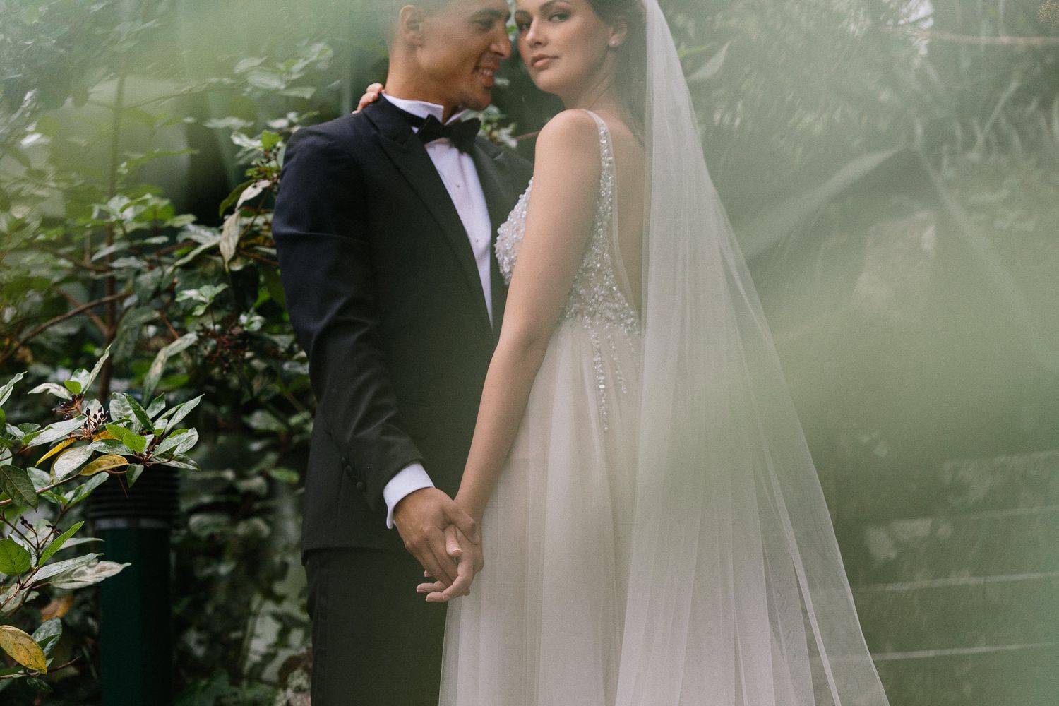 Wedding couple sharing intimate moment in lush garden with flowing veil.