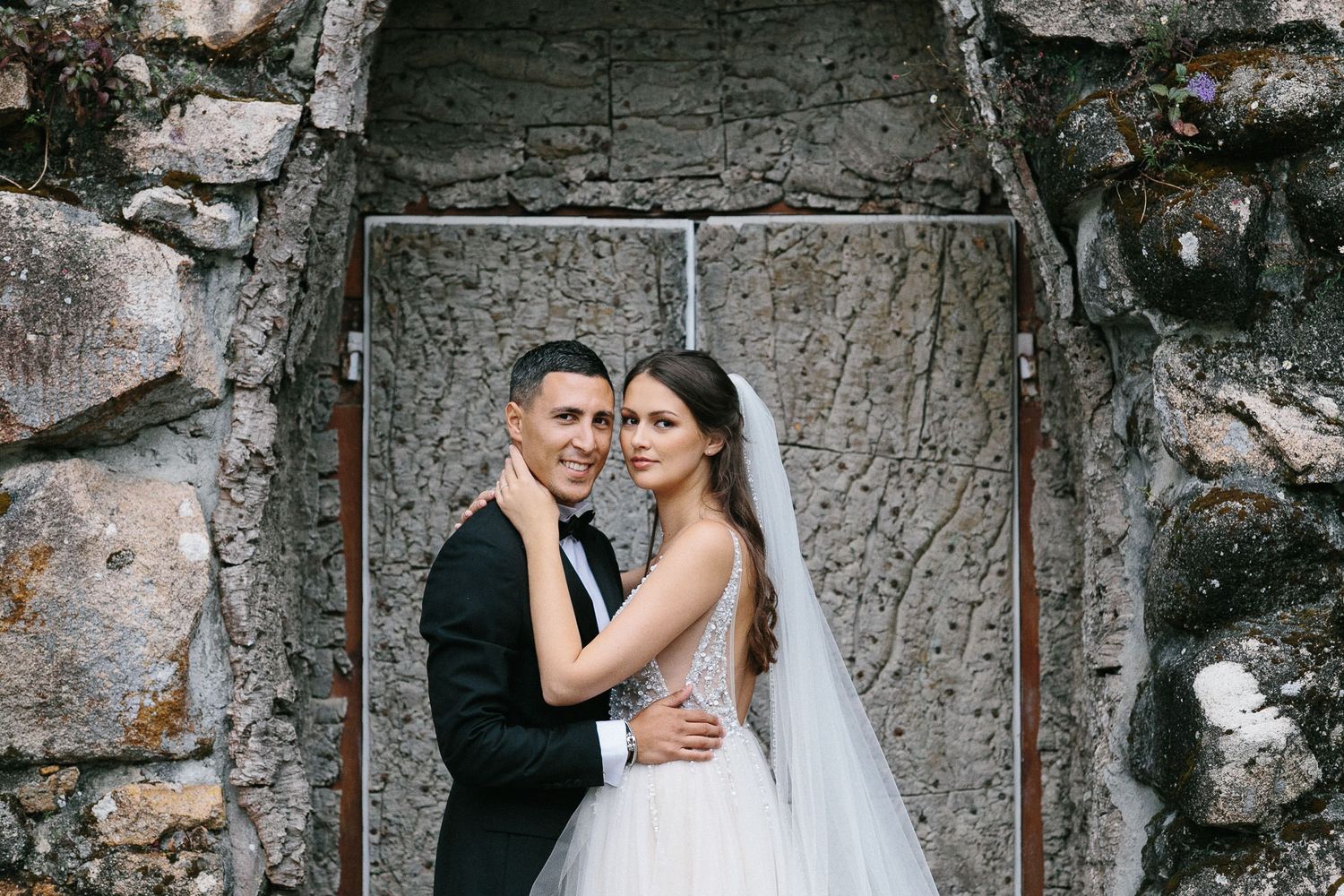 Elegant couple pose in stone archway during wedding photoshoot.