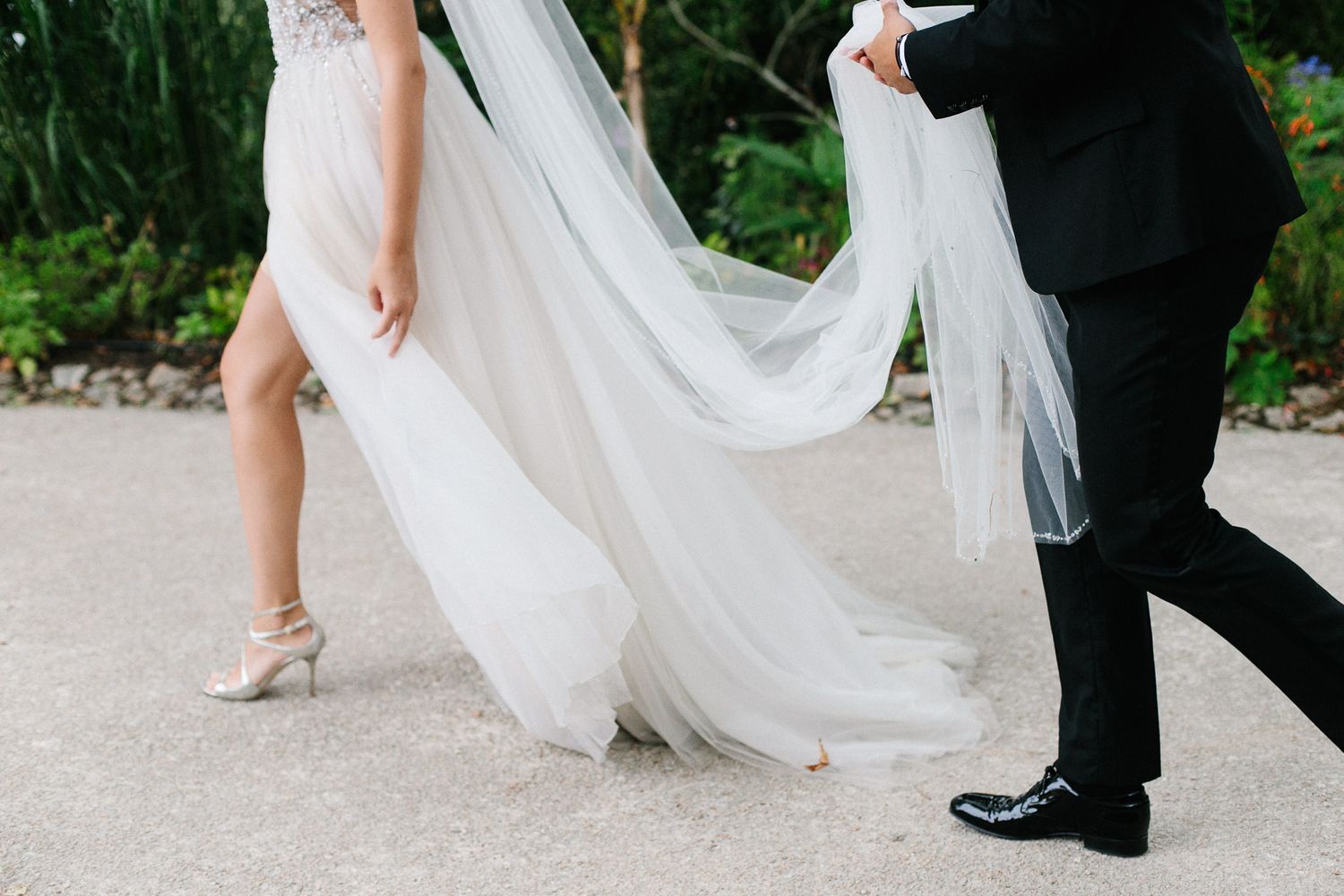 Elegant wedding photo showing bride's flowing white dress and groom's black shoes during an outdoor ceremony.