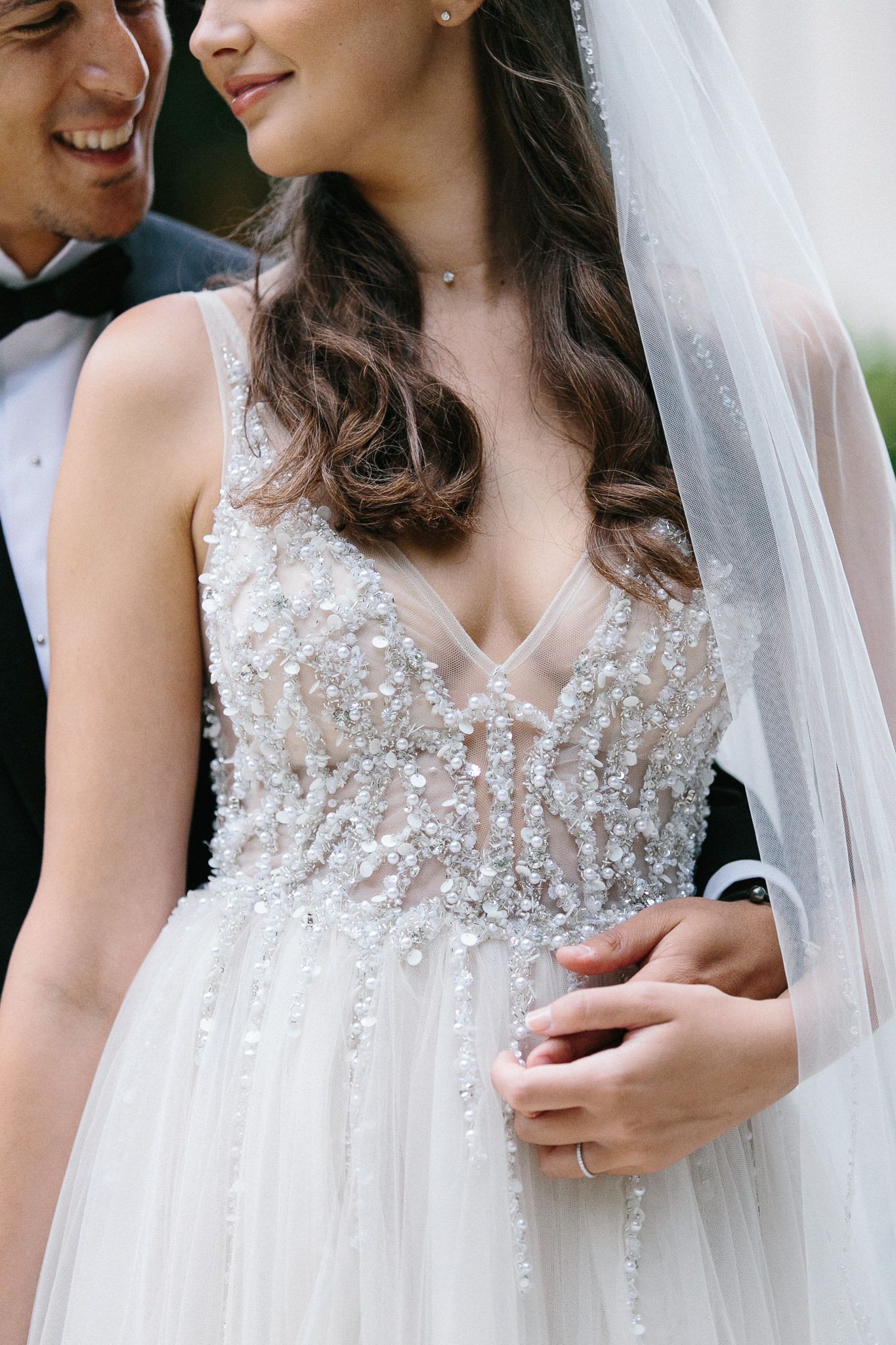 Close-up detail of intricate beading on wedding dress bodice with tulle and veil.