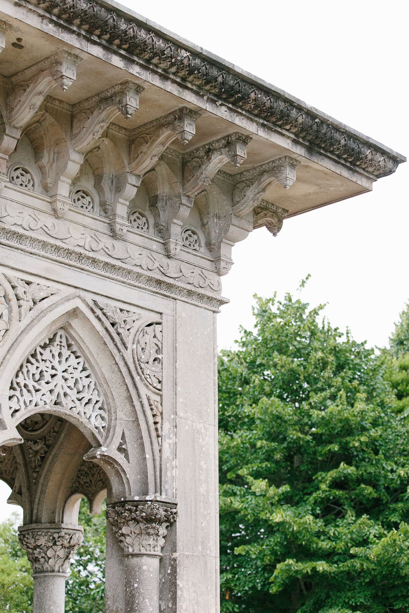 Detailed Gothic architectural elements with ornate stone carvings and arches against green foliage.