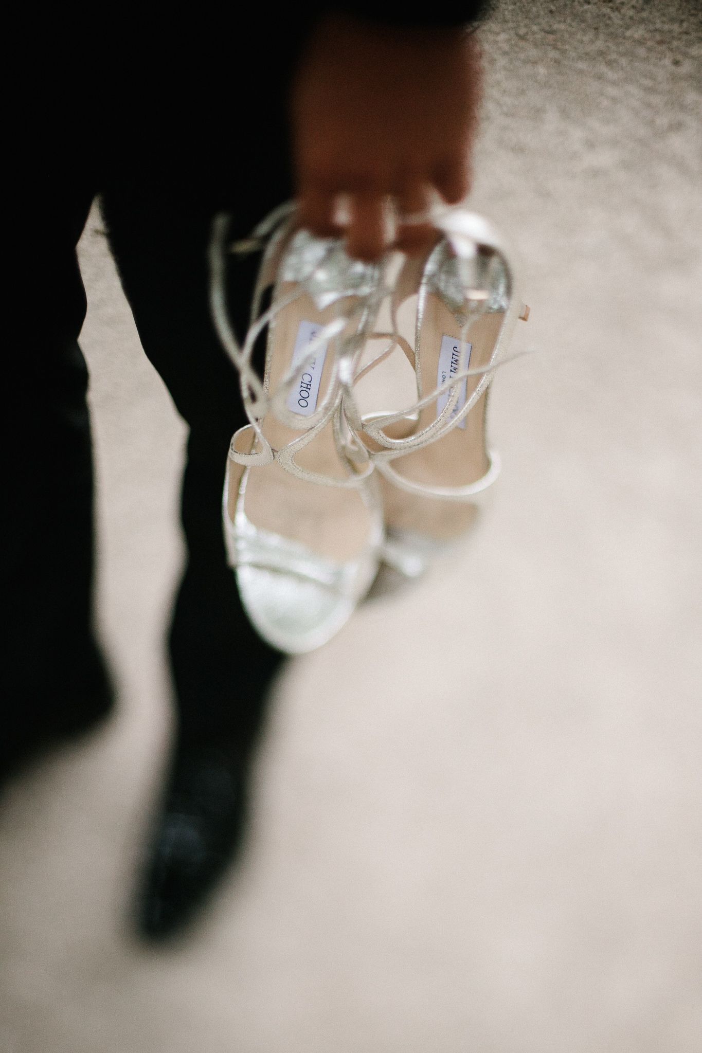 Elegant white bridal sandals with straps photographed on a blurred background.