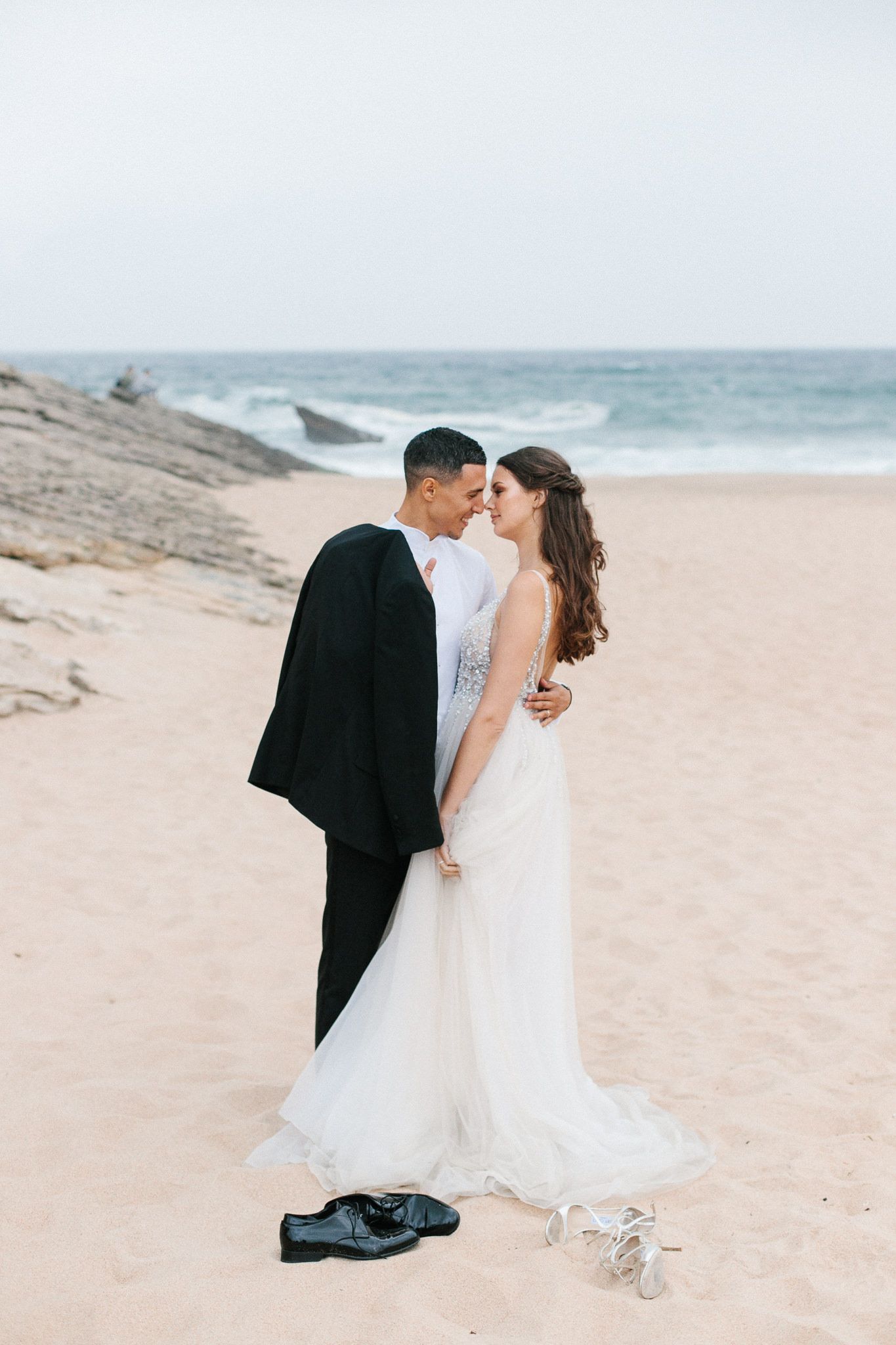 Newlyweds sharing a romantic moment on a beach with ocean waves in the background.