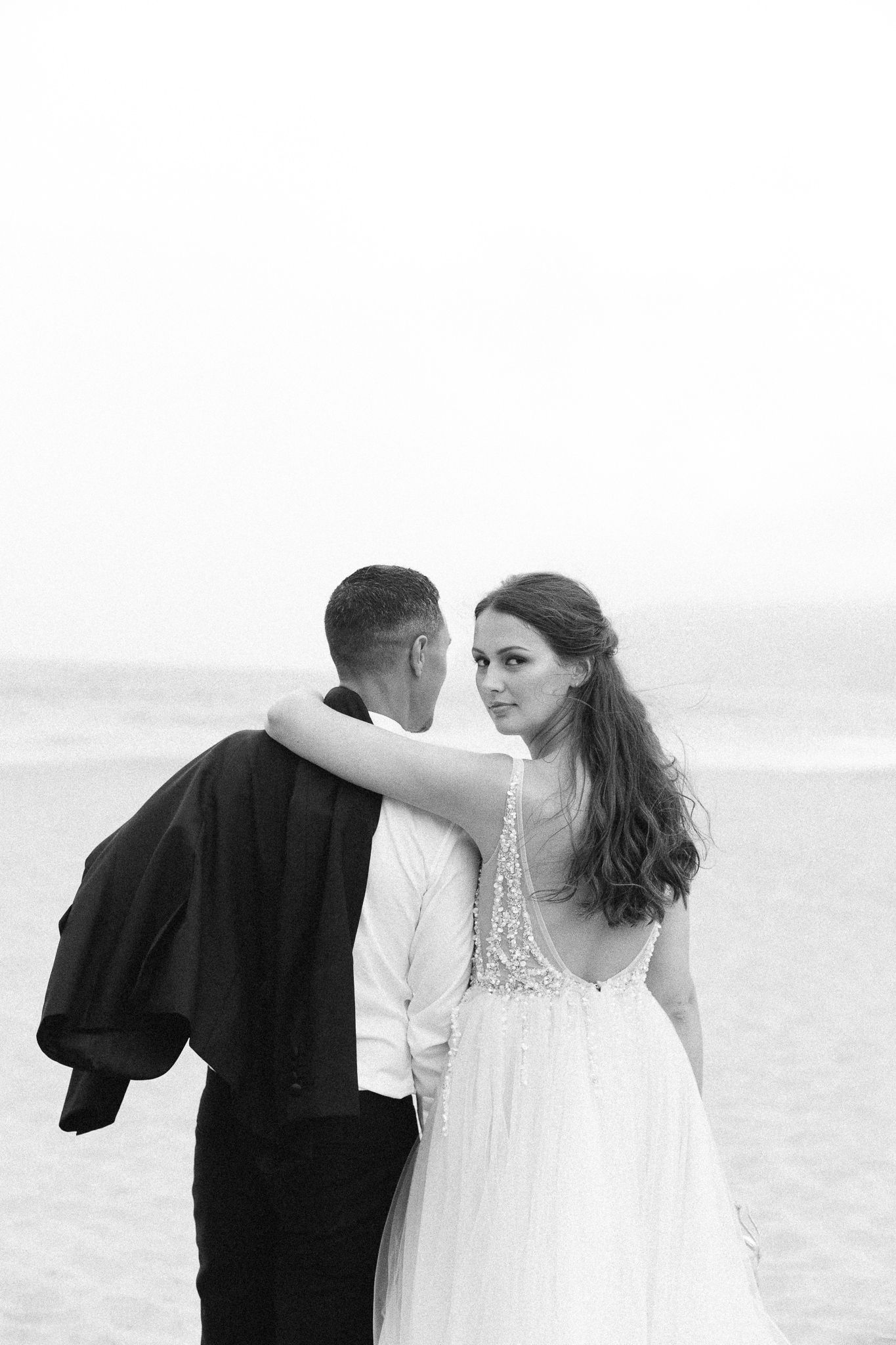A black and white portrait of newlyweds embracing on a sandy beach.