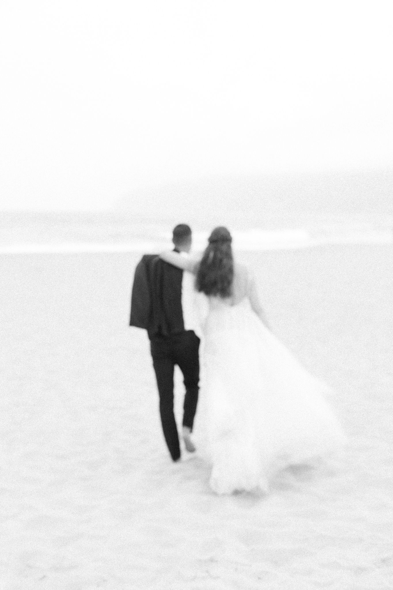 Black and white image of newlyweds walking together on a beach.