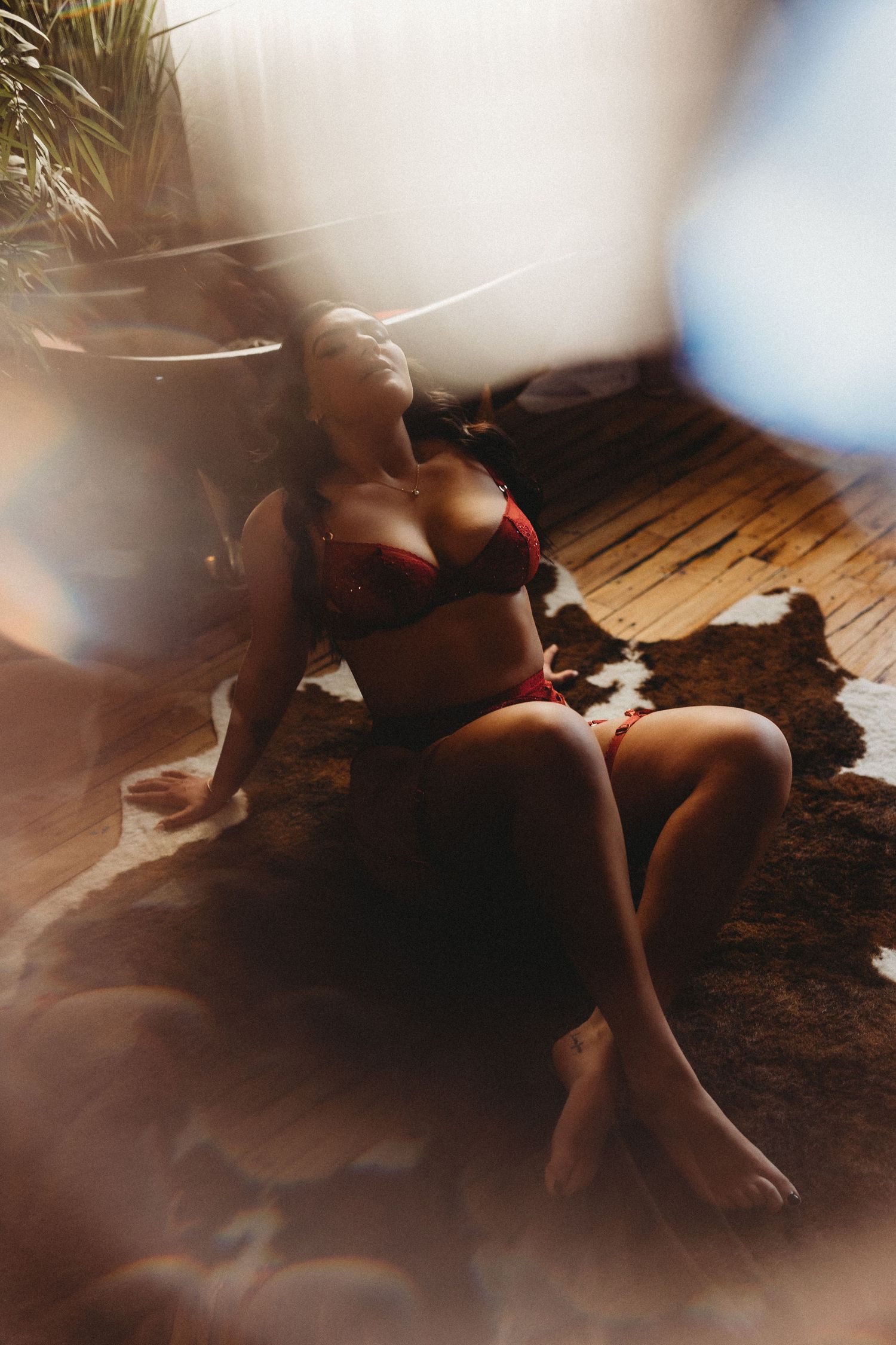 Artistic boudoir photo with soft lighting shows a silhouette seated on wooden flooring in moody atmosphere.