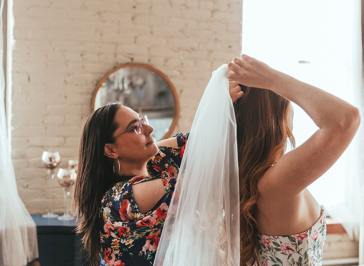 Mallory fixing a cathedral bridal veil with a bride wearing a white and light pink floral corset.