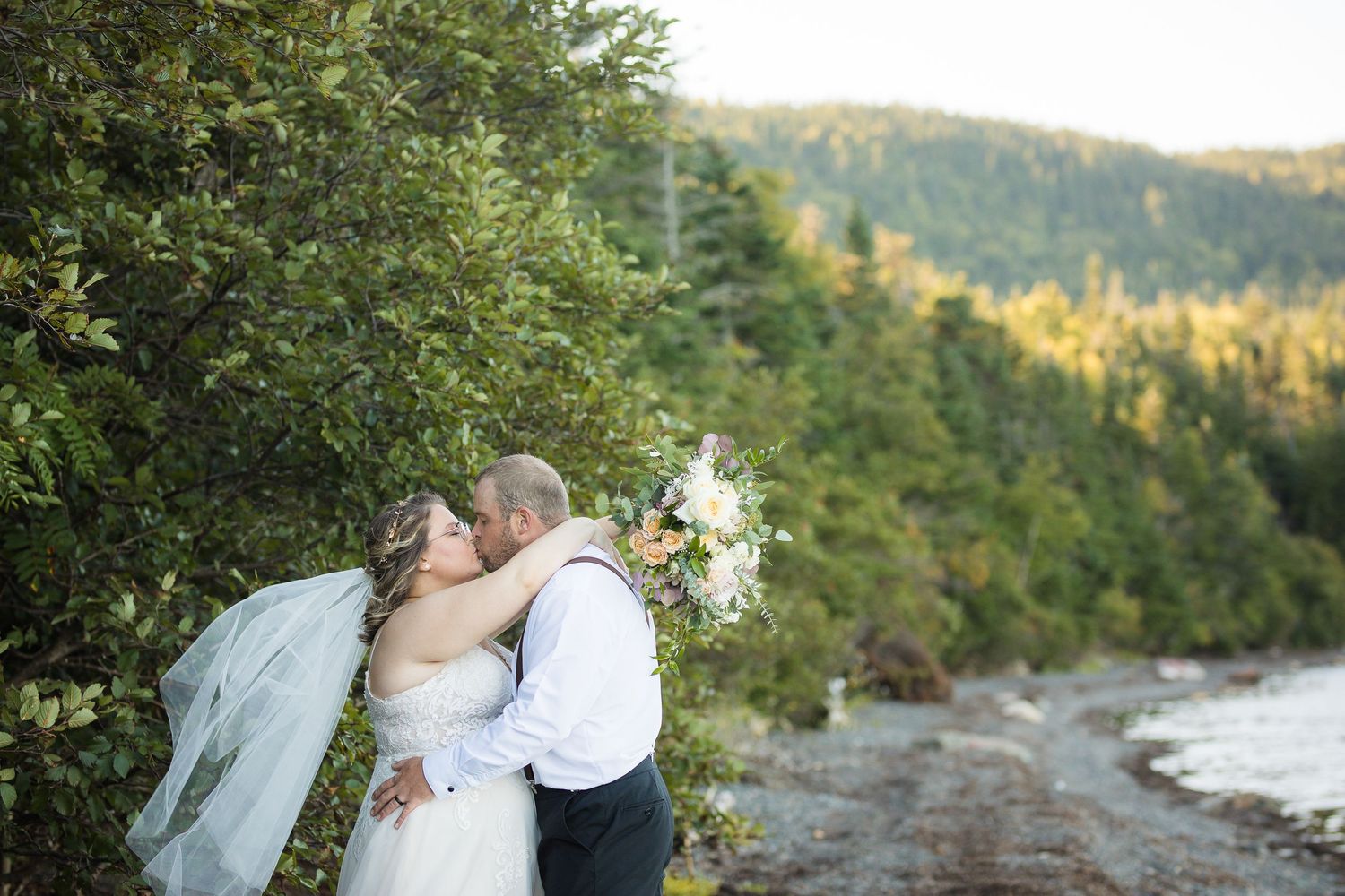 Intimate wedding moment captured against scenic mountain and waterfront backdrop.