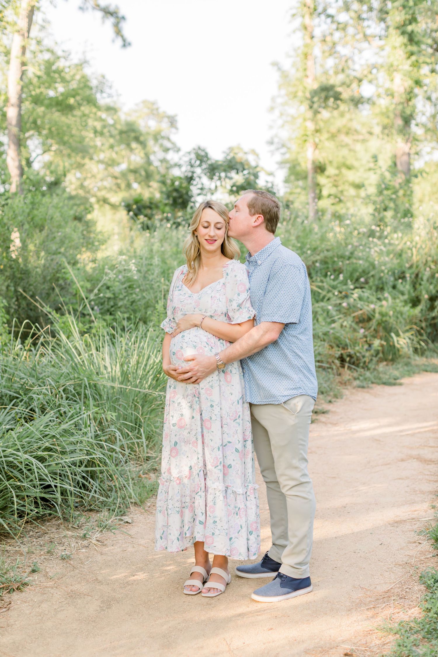 A loving embrace between expectant parents on a sunlit forest path.