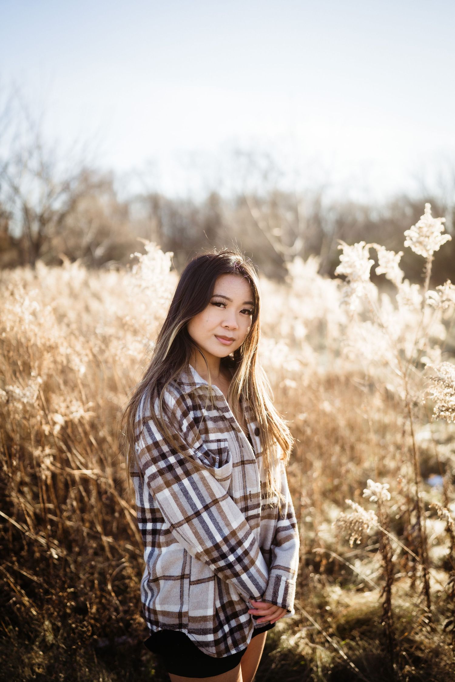 Person in plaid flannel shirt poses in golden field at sunset.