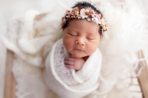 Newborn baby wrapped in white with delicate floral headpiece.
