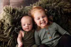 Siblings lying on fluffy dark rug during lifestyle portrait session.