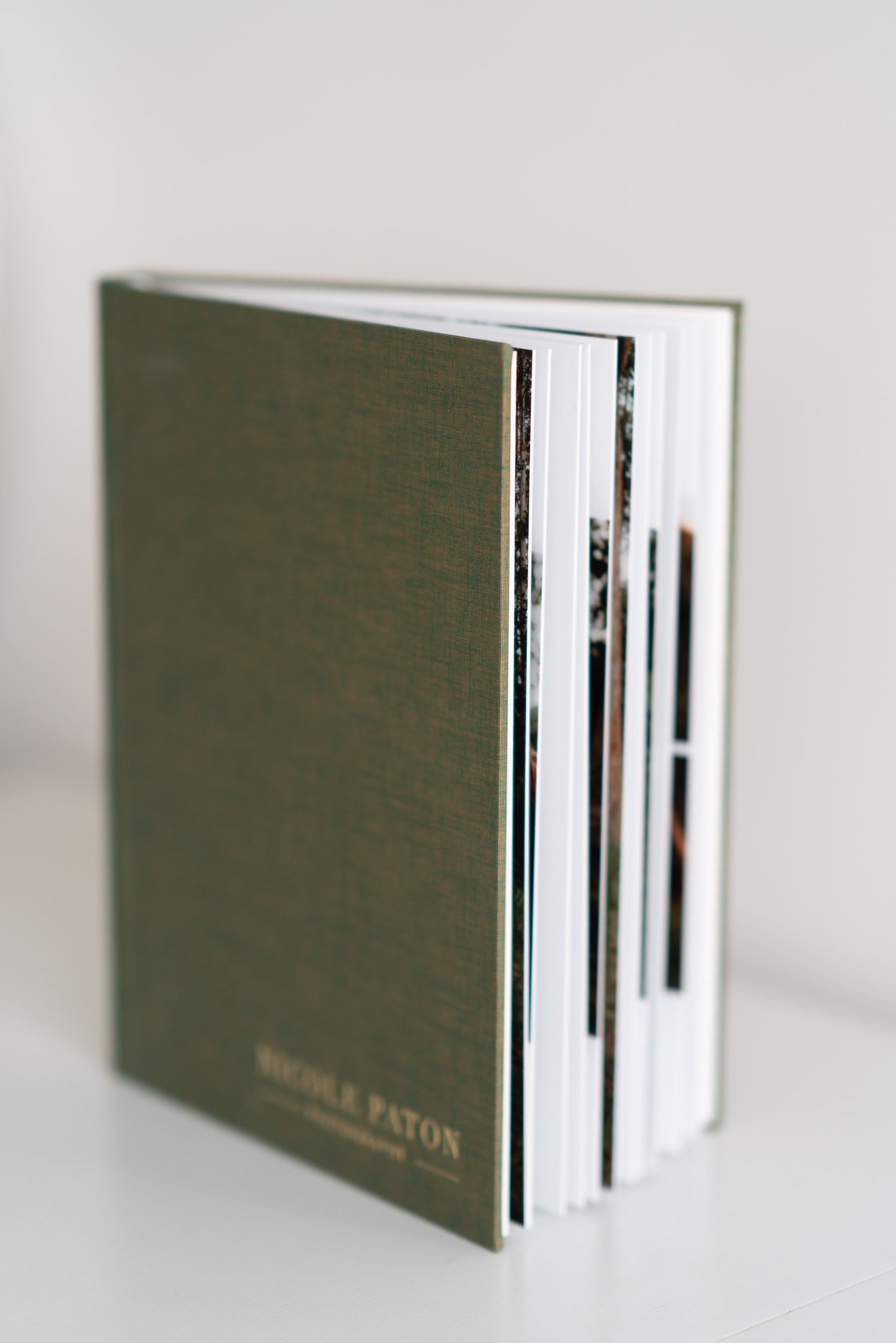 green linen album with logo on bottom right corner sits on the table with pages on display to see thickness of the pages