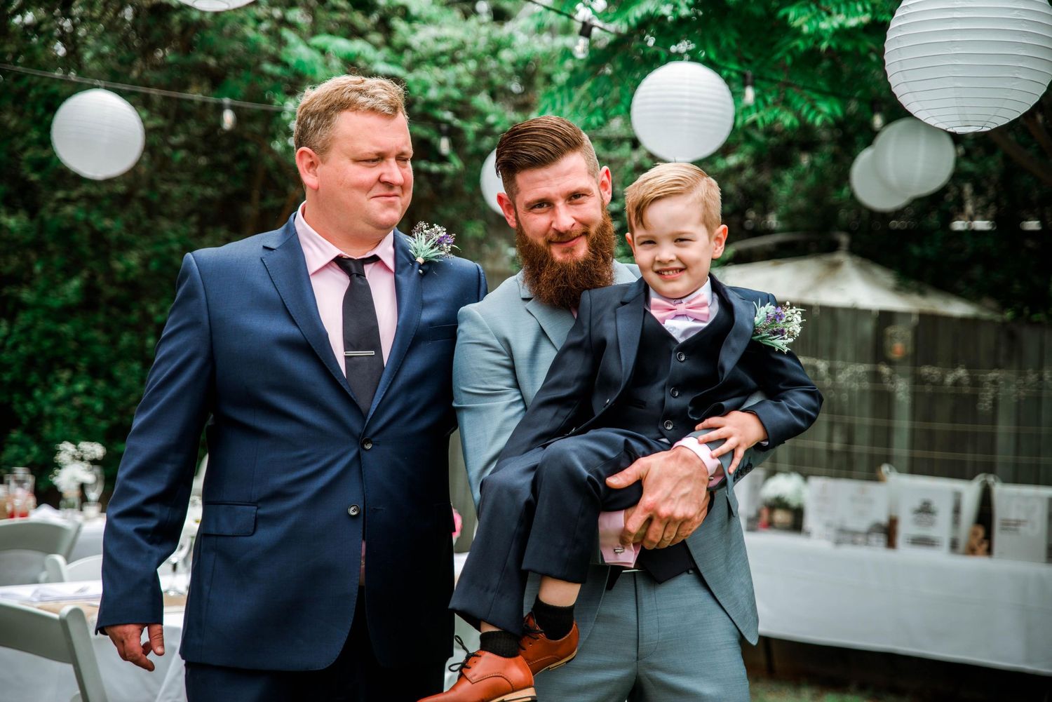 Three guests share an intimate moment at an outdoor wedding with white lantern decorations.