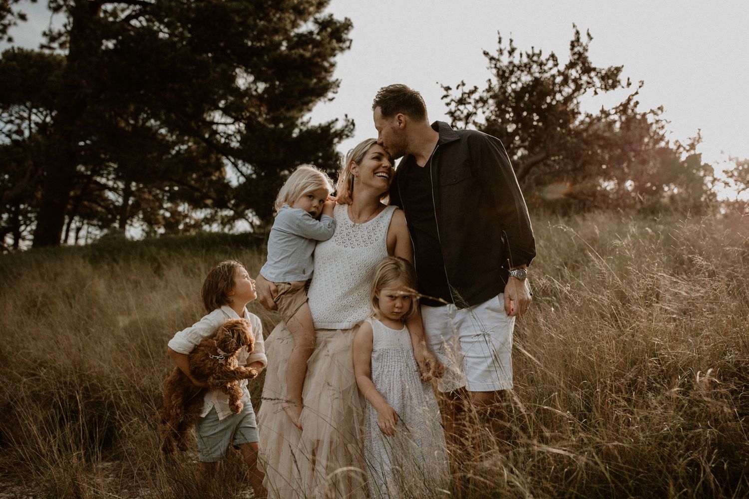 A golden hour family portrait in tall grass with dog at sunset.