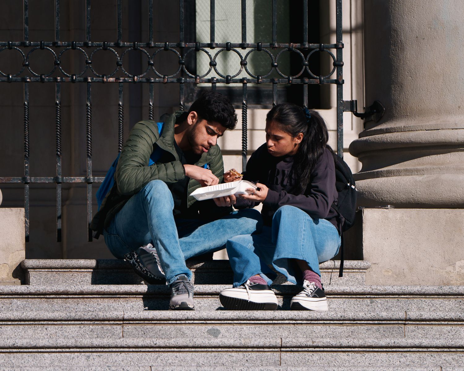 A man and a woman having lunch on the steps of a art museum, street photography.