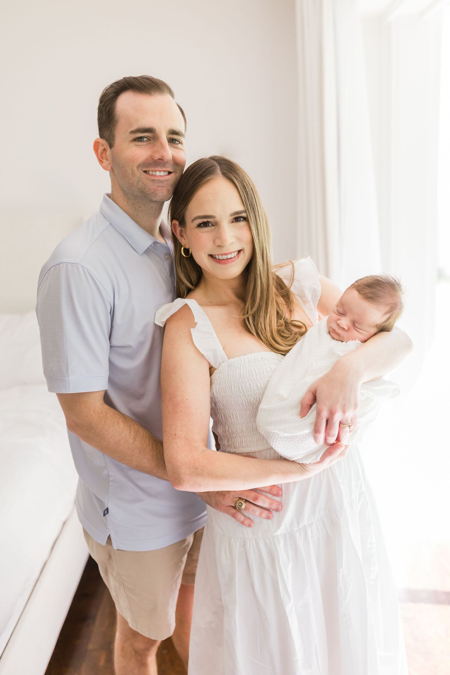 Family portrait with newborn baby in bright white interior setting.