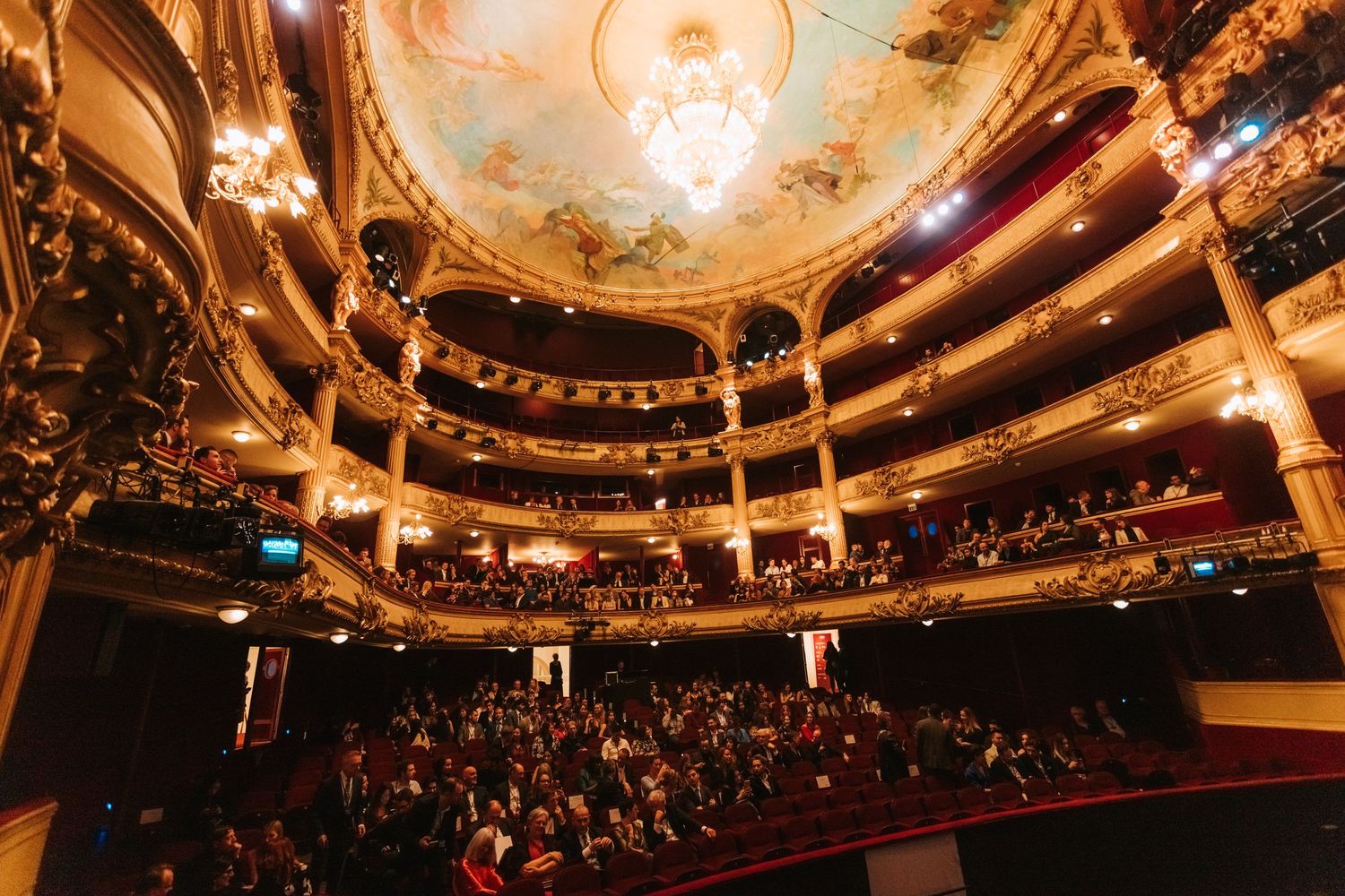 Ornate theater interior with beautiful painted ceiling and multiple balcony levels filled with audience members.