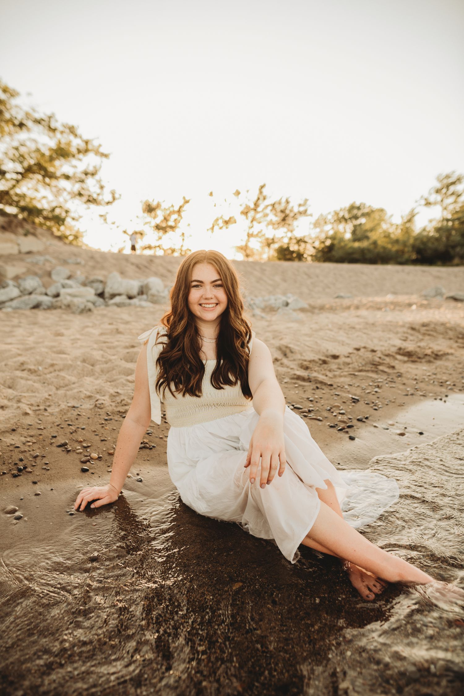 Artistic sunset photoshoot on sandy beach with flowing white dress.